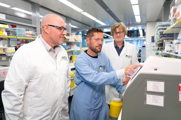 Three individuals wearing lab coats in discussion in a lab. 
