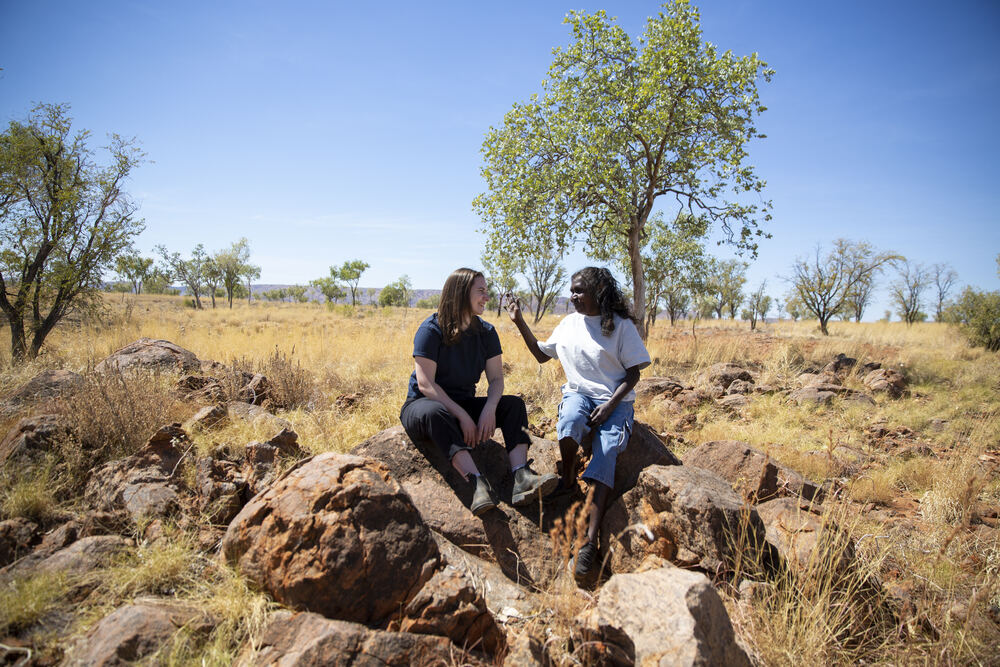 Two women sitting on large rocks in a grassy field, enjoying the outdoors.