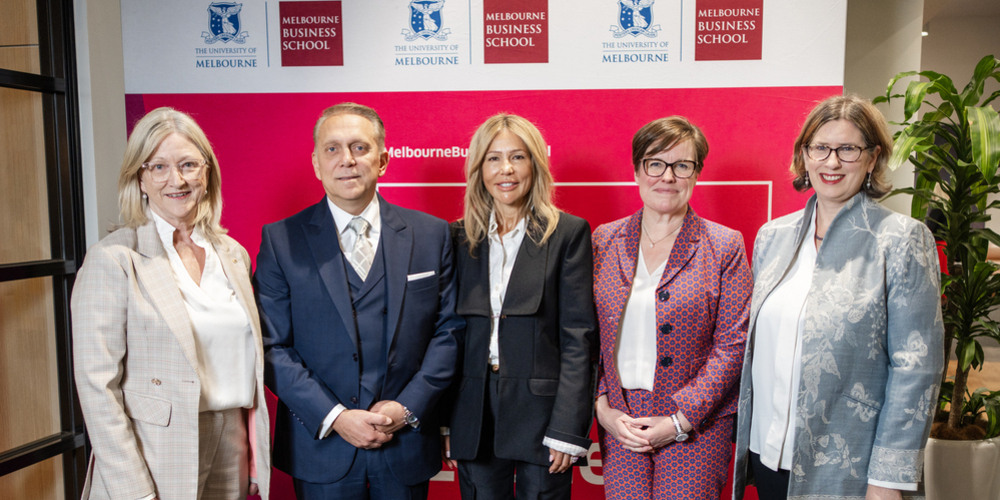 Five people are positioned next to each other in front of a striking red wall, each displaying cheerful smiles.