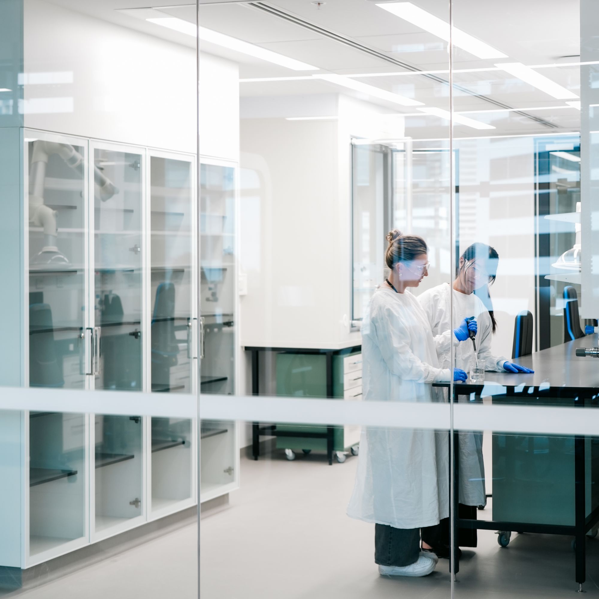 People working at a bench inside a laboratory behind glass walls