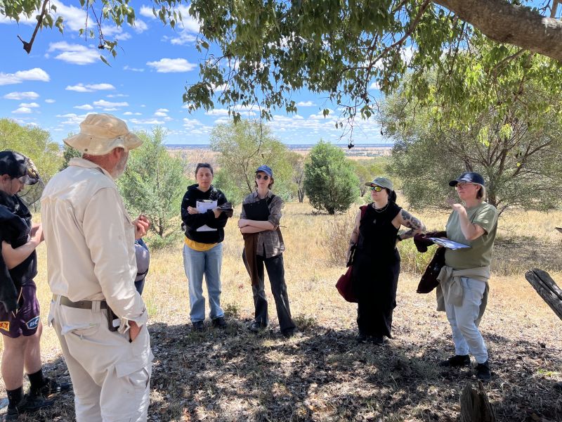 People gathered outdoors in a bushland area listening to a speaker