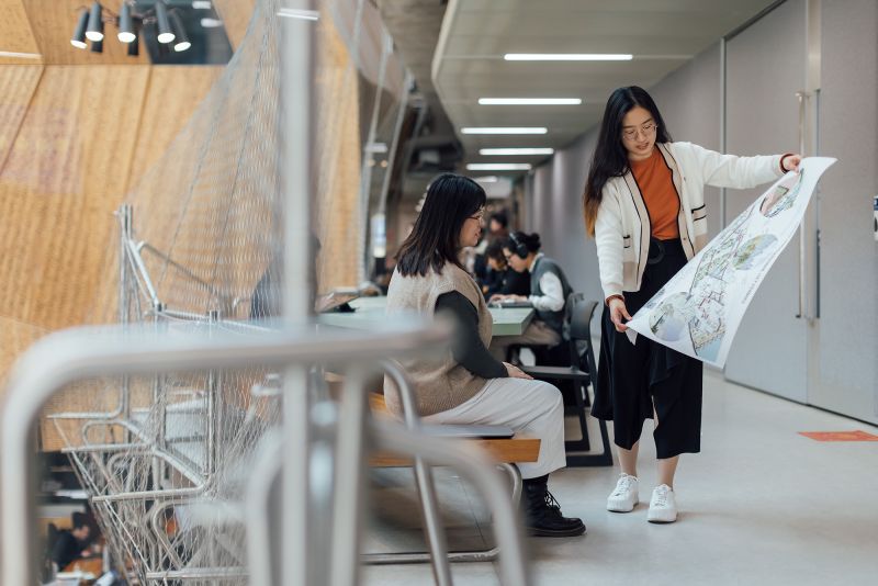Two female MSD students examining a large plan in the Glyn Davis Building