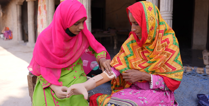 Kainat (left) guides Habiba (right) on how to use her new prosthetic arm.