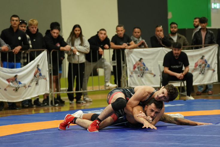A wrestler is on his back, facing a tough challenge in the heat of a wrestling match.