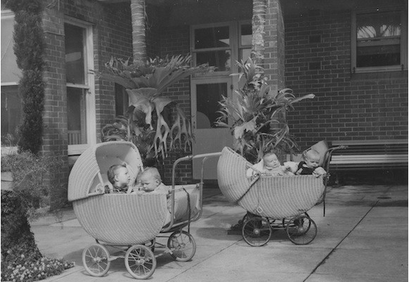 Black and white image of two wicker strollers with babies in them.
