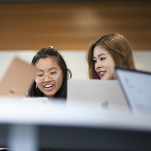 Two female students looking at their laptops and smiling together.
                                class=