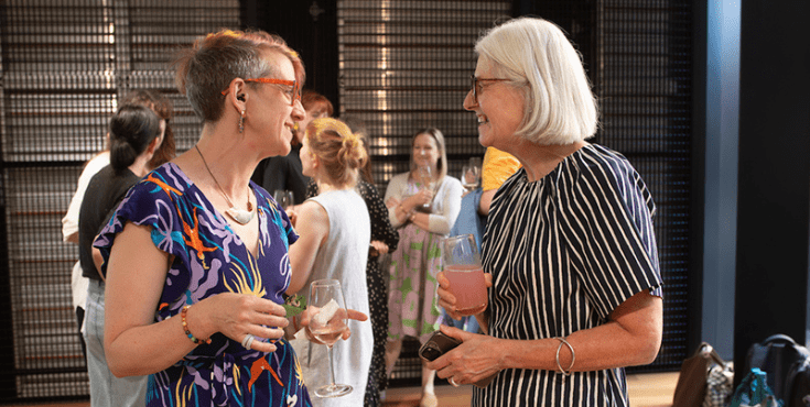 Two women catching up at an event, smiling with drinks in hand