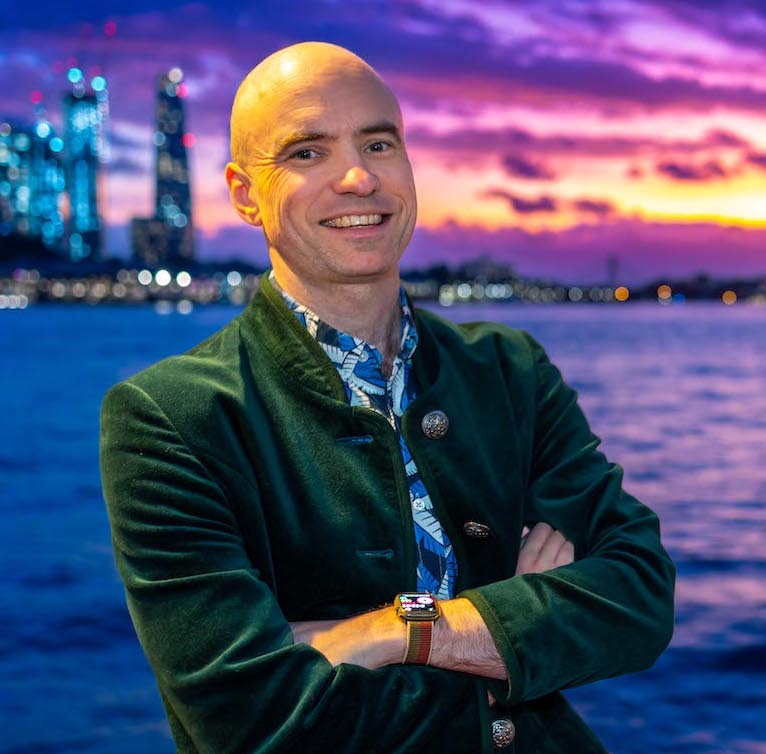 Ben Loveridge stands in front of a colourful sunset wearing a green velvet jacket.
