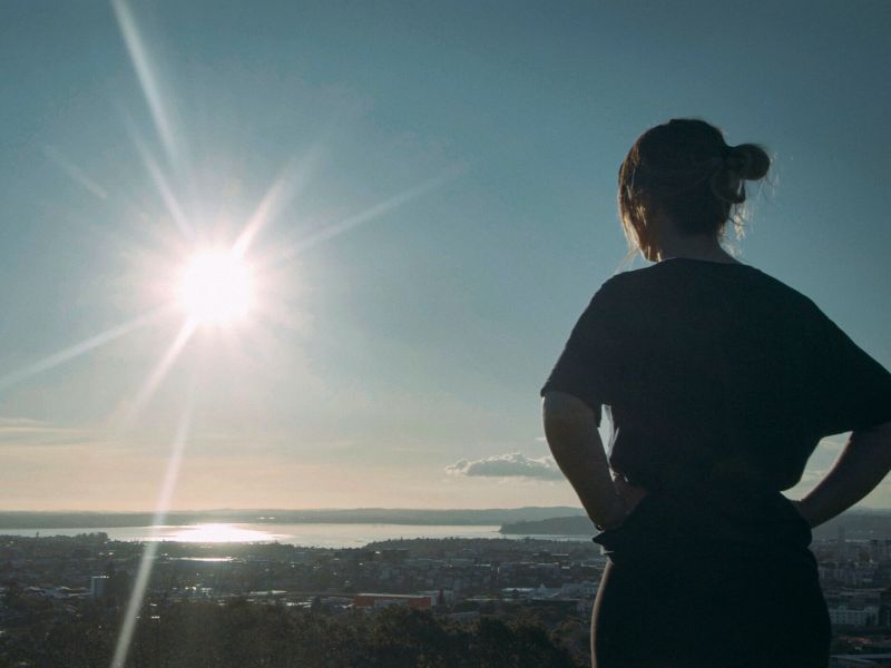 Healthcare worker standing in the sun on a hill with their hands on their hips and their back to the camera, looking out.