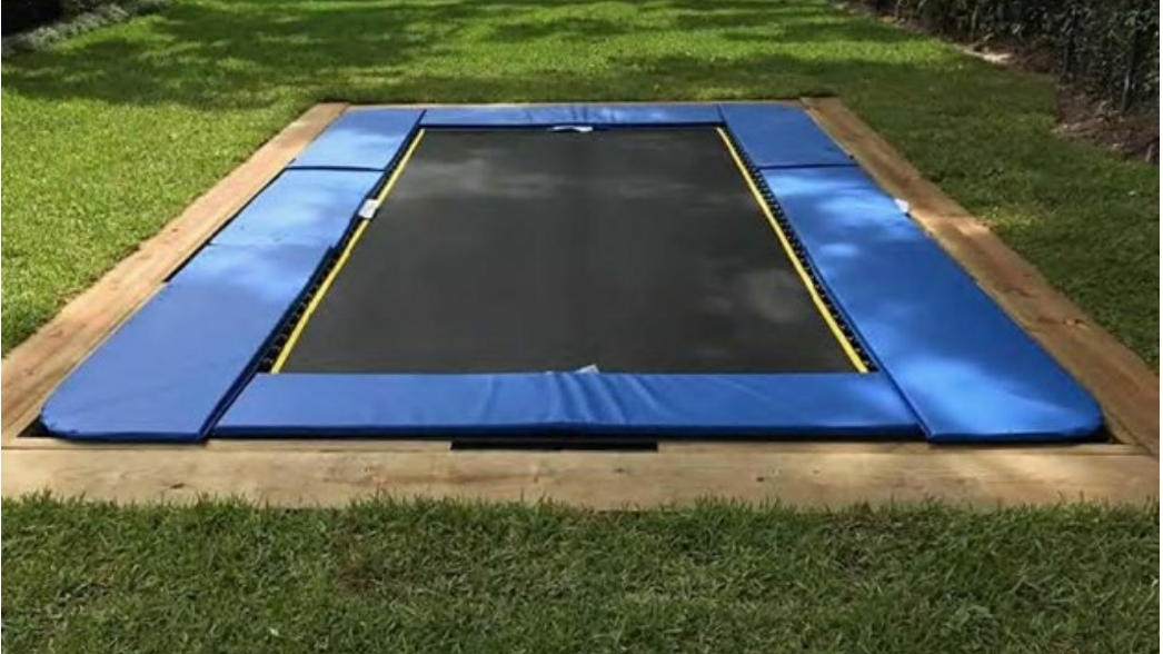 A trampoline installed with a wooden border surrounding it in a grassy lawn