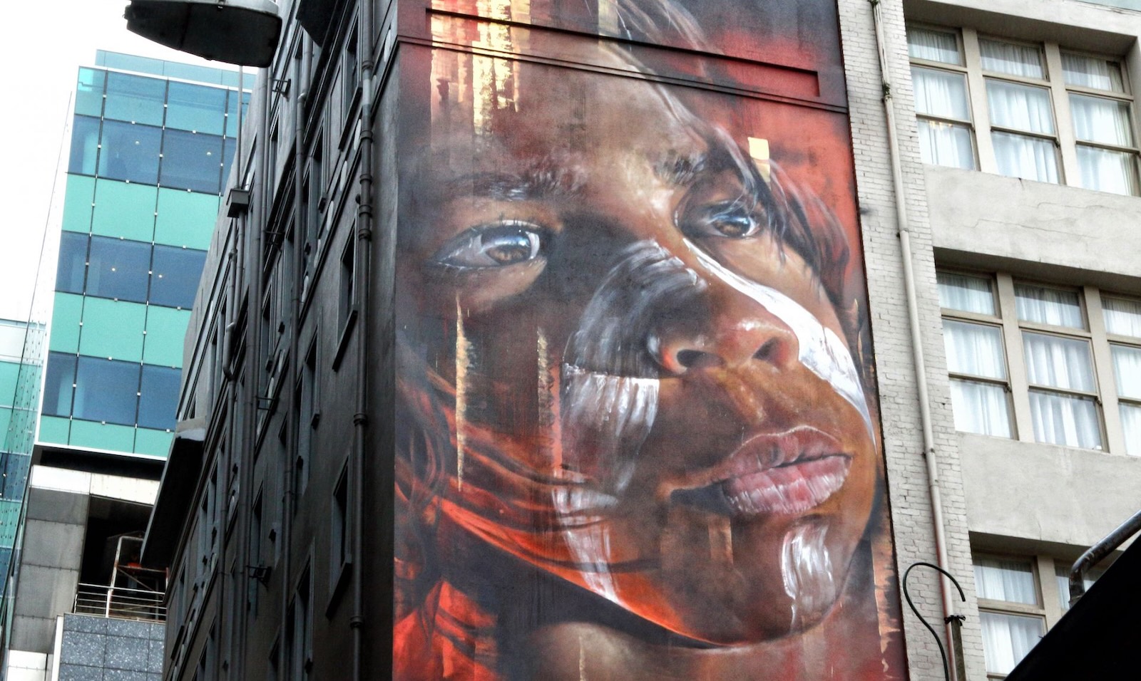 Large street art portrait of an Indigenous boy with white paint markings on his face.
