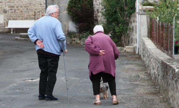 Image of an elderly couple supporting their backs and walking with canes. 