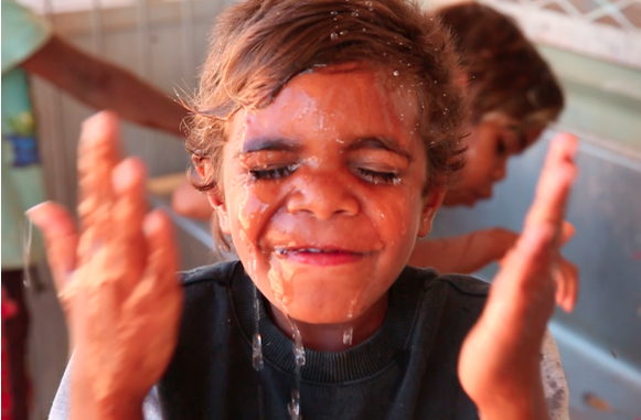 Image of a young Indigenous boy splashing water on his face.