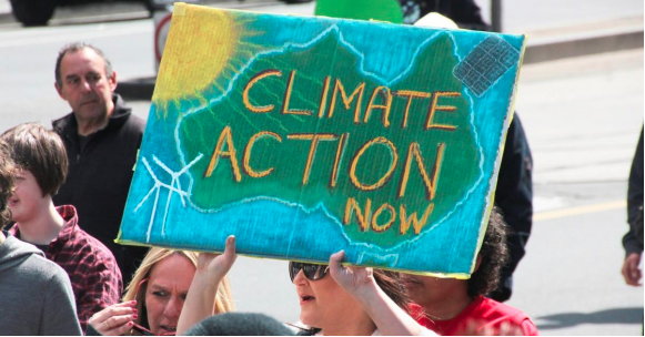 Image of a protester holding up a sign which reads Climate Action Now.