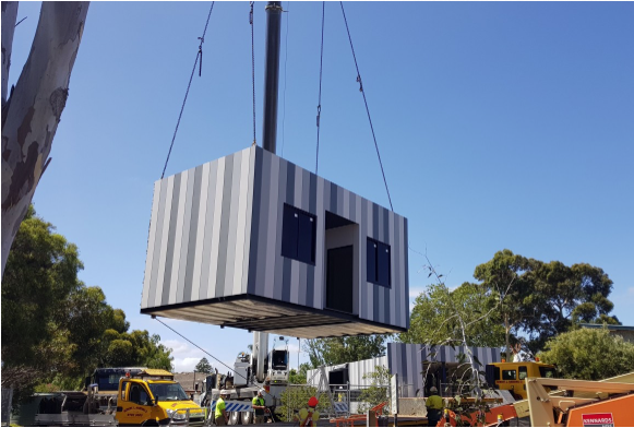 Image of a portable prefabricated structure being lowered by a crane.
