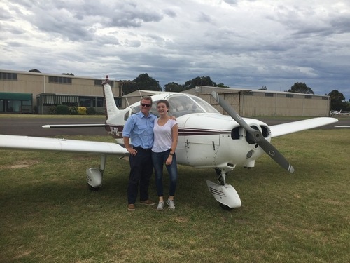 Two people stand side by side in front of a small aircraft.