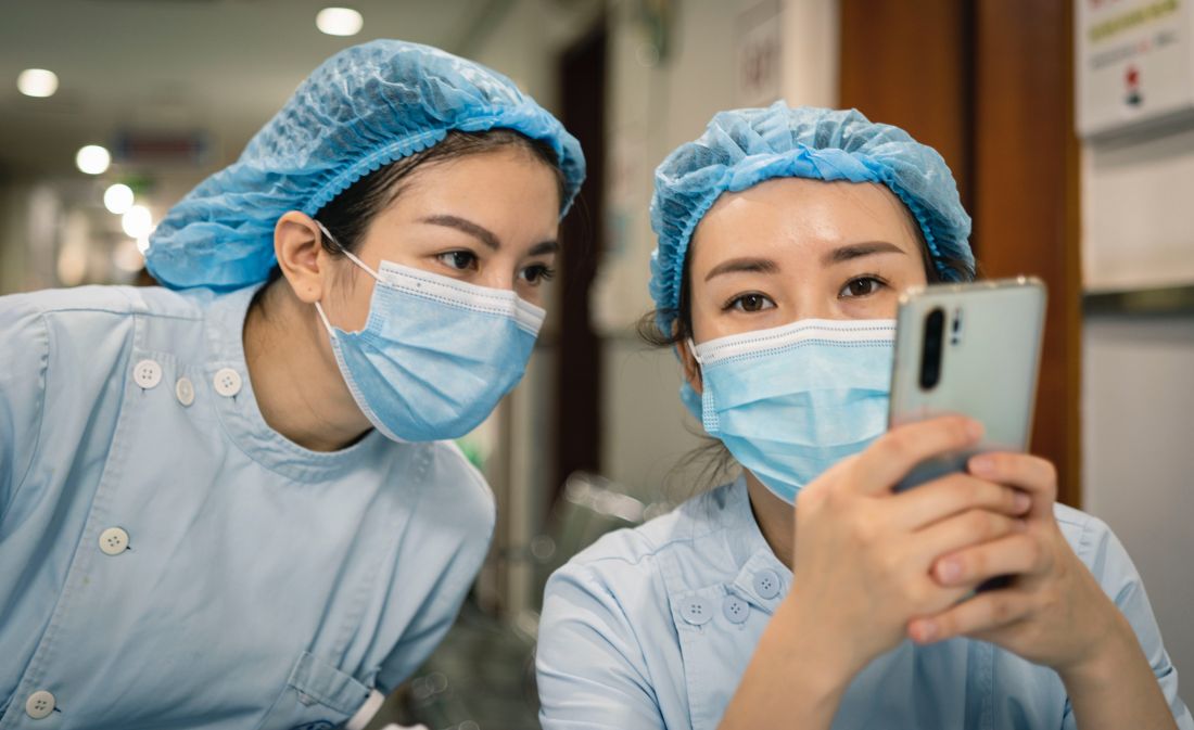 Two female healthcare workers in PPE look at a phone