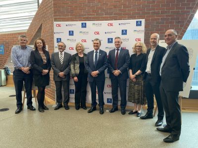 Nine people stand in front of a promotional banner with CSL, WEHI and University of Melbourne branding.