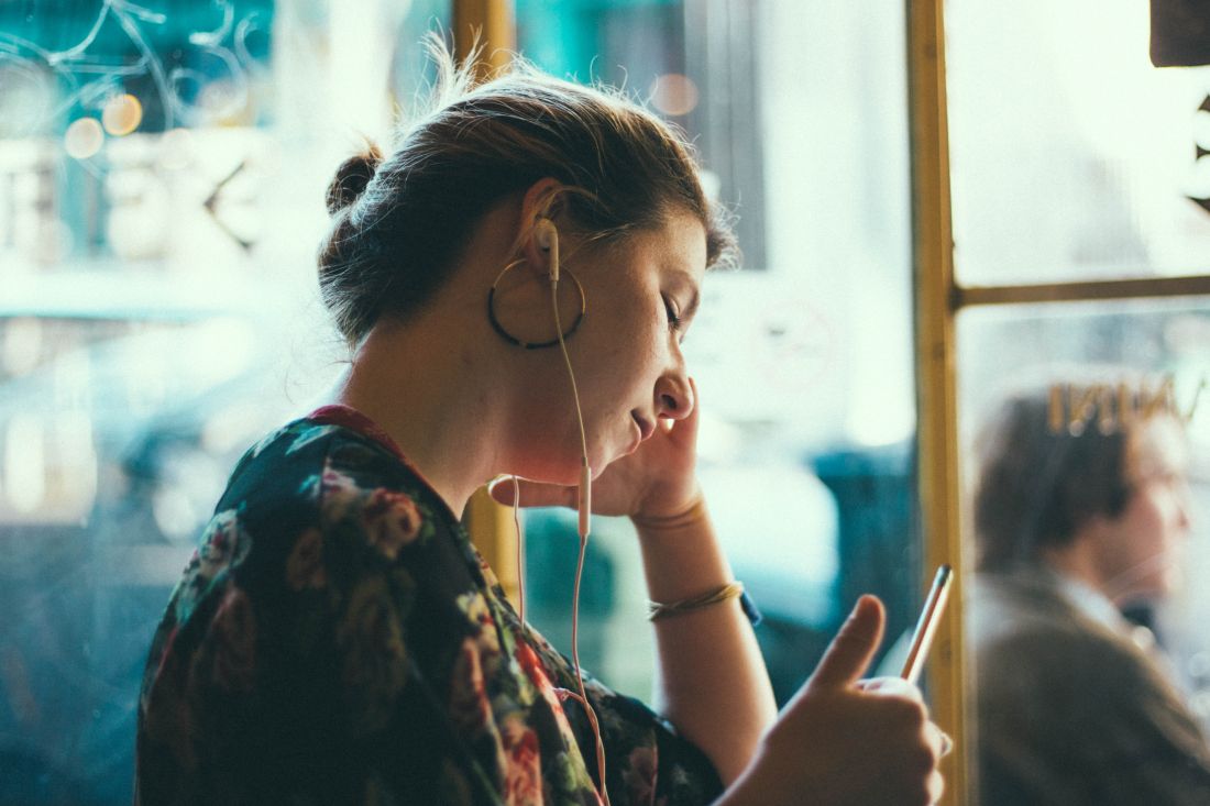 A young woman sits with earphones in and a pencil in her hand