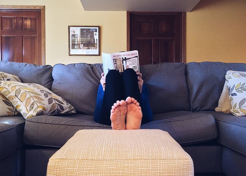 Person sitting on the couch reading a newspaper, feet on the coffee table