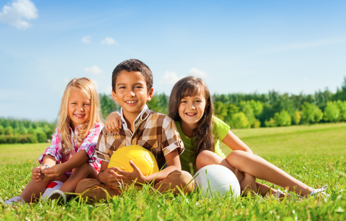Three smiling kids sitting a field