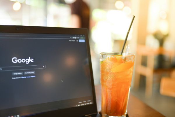 An orange drink in a tall glass next to a laptop with a dark screen and the Google search engine
