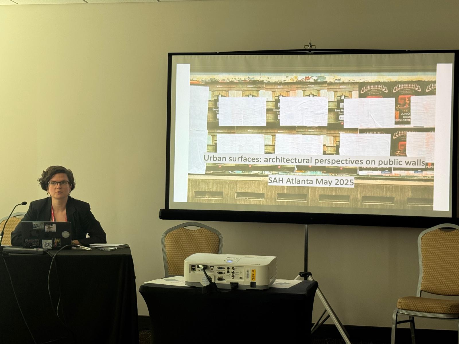 Sab Sabina Andron presenting in front of a slide with the title 'Urban surfaces: architectural perspectives on public walls