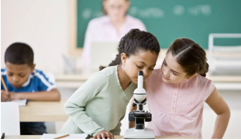 Image of two young girls working looking into a microscope together.
