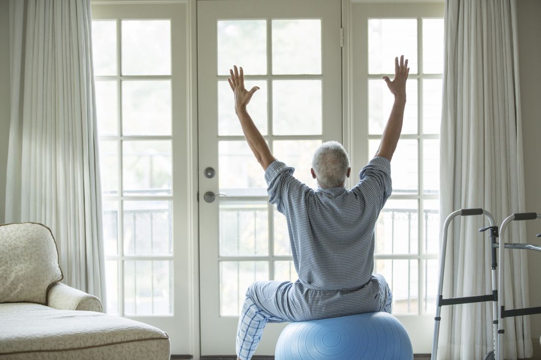 Older man sitting on an exercise ball facing a window and stretching